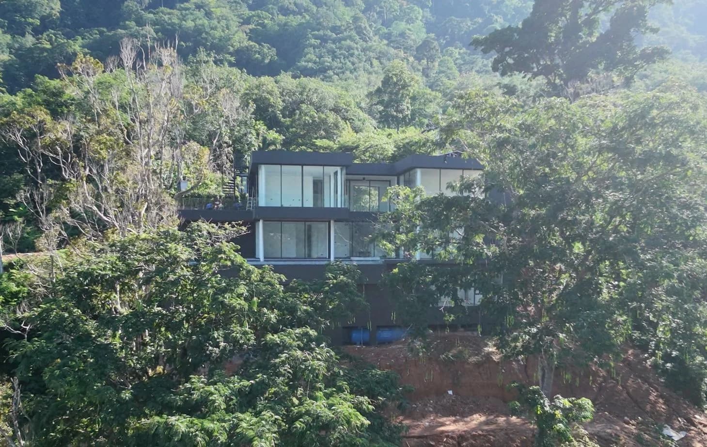 Perch House, exterior from the hillside showing the three-floor glass facade above the Kamala valley